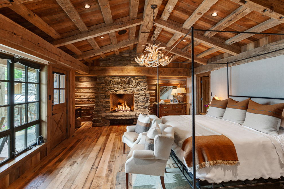Cette photo montre une chambre parentale montagne en bois avec un manteau de cheminée en pierre et poutres apparentes.