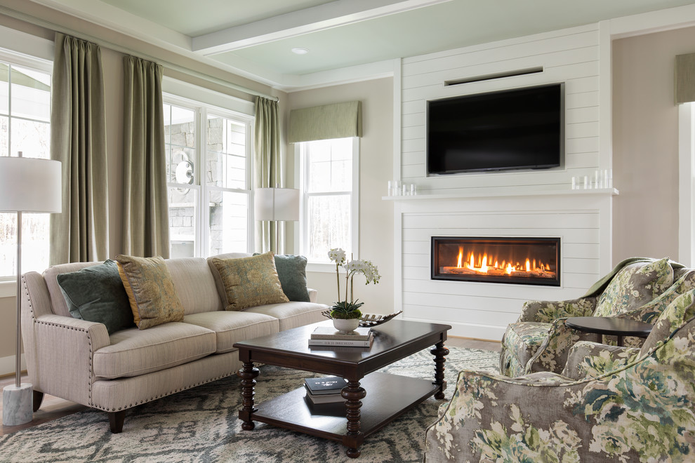 Photo of a traditional family room in Richmond with beige walls, medium hardwood floors, a ribbon fireplace, a wood fireplace surround, a wall-mounted tv and brown floor.