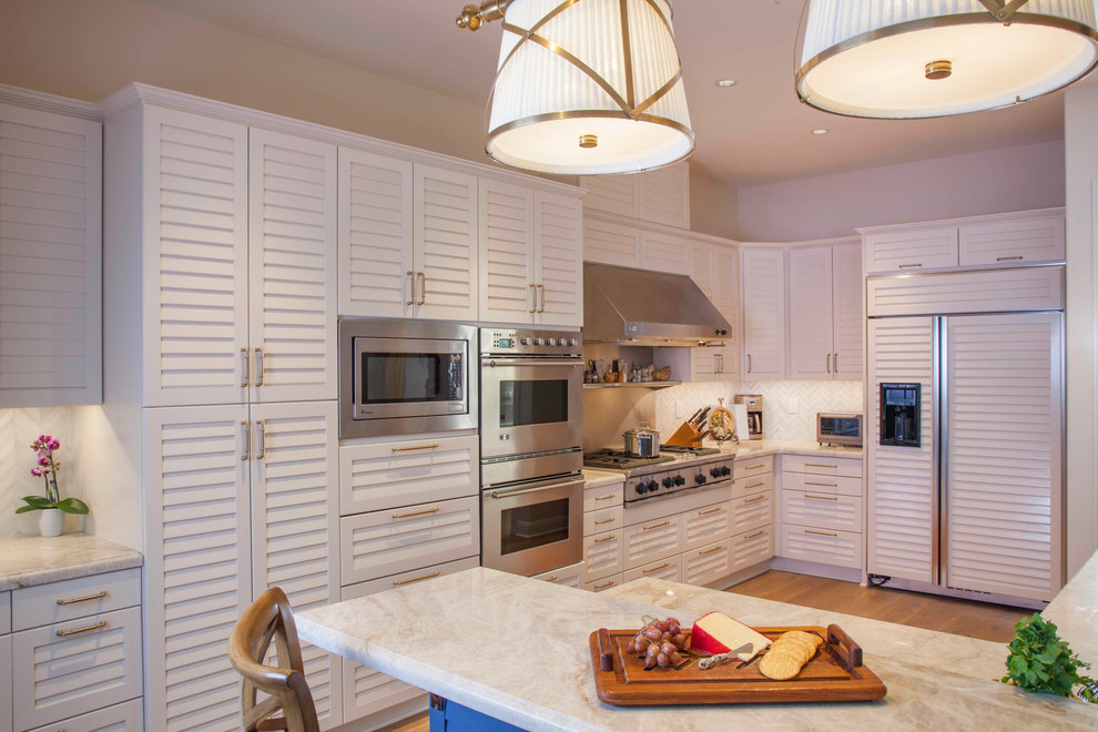 Inspiration for a mid-sized beach style single-wall eat-in kitchen in San Diego with louvered cabinets, white cabinets, marble benchtops, white splashback, stainless steel appliances, light hardwood floors, with island, brown floor, white benchtop and marble splashback.