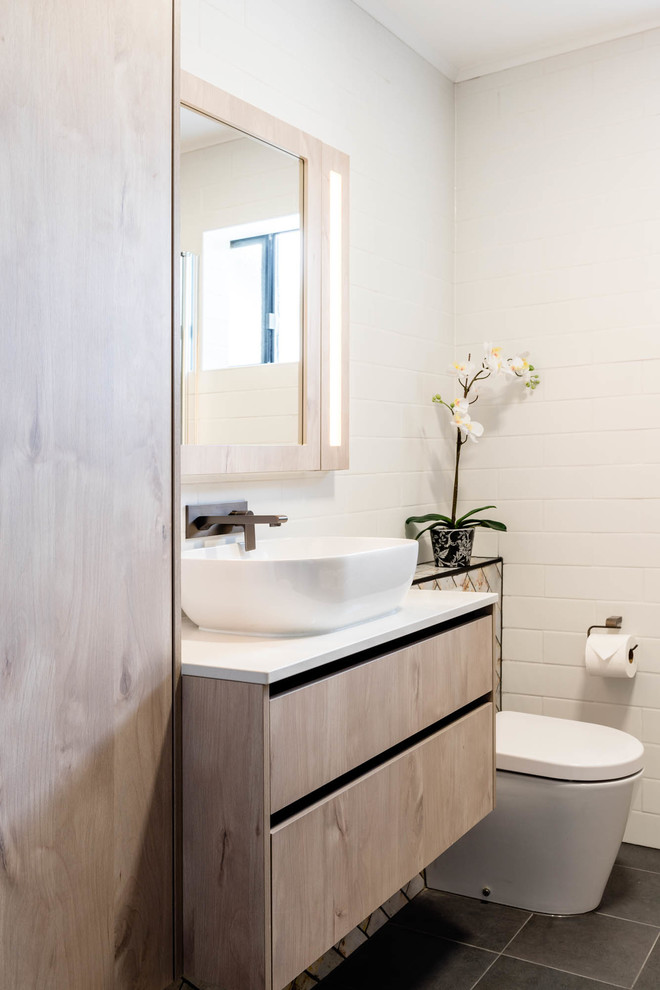 Mid-sized contemporary 3/4 bathroom in Brisbane with flat-panel cabinets, light wood cabinets, a wall-mount toilet, white tile, subway tile, ceramic floors, a vessel sink, engineered quartz benchtops, black floor and white benchtops.