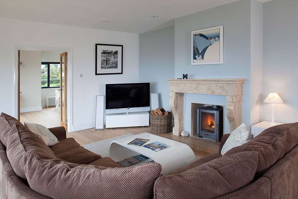 Photo of a small contemporary enclosed living room in Cornwall with multi-coloured walls, light hardwood floors, a wood stove, a plaster fireplace surround and a freestanding tv.