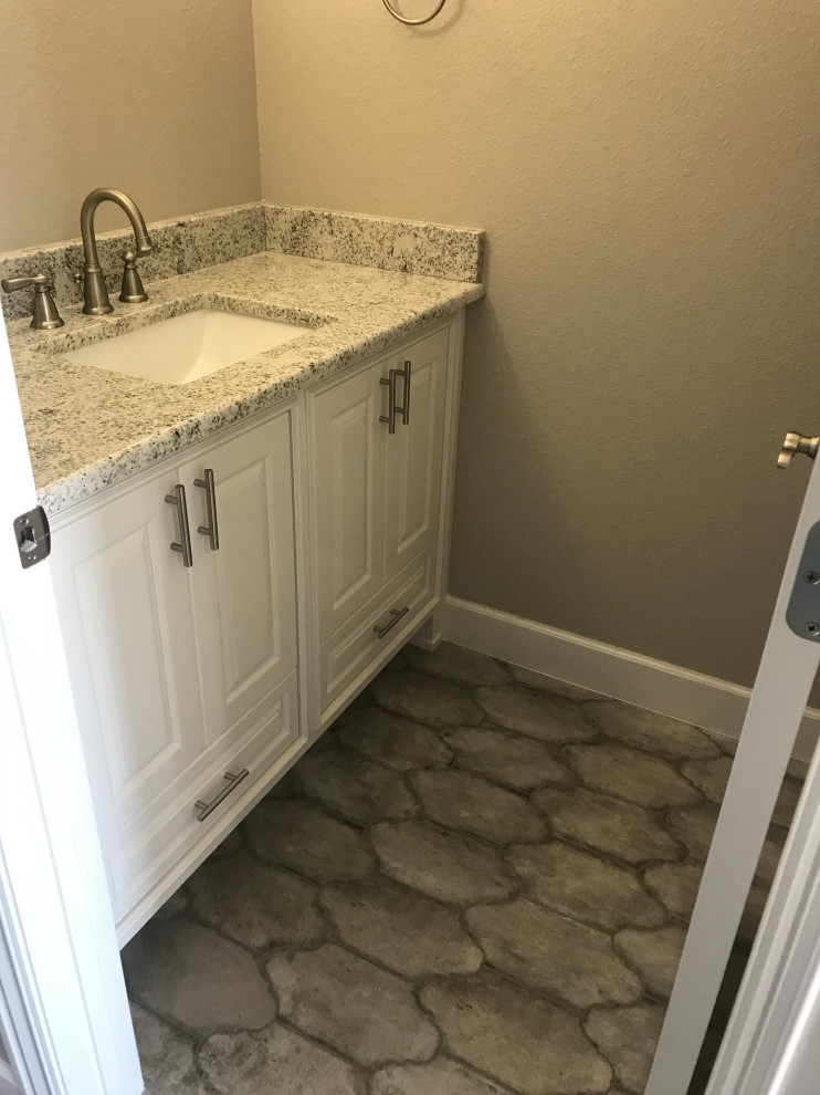 Cette photo montre un petit WC et toilettes avec un placard à porte shaker, des portes de placard blanches, un mur gris, un sol en carrelage de céramique, un plan de toilette en granite, un sol gris, un plan de toilette multicolore et meuble-lavabo encastré.