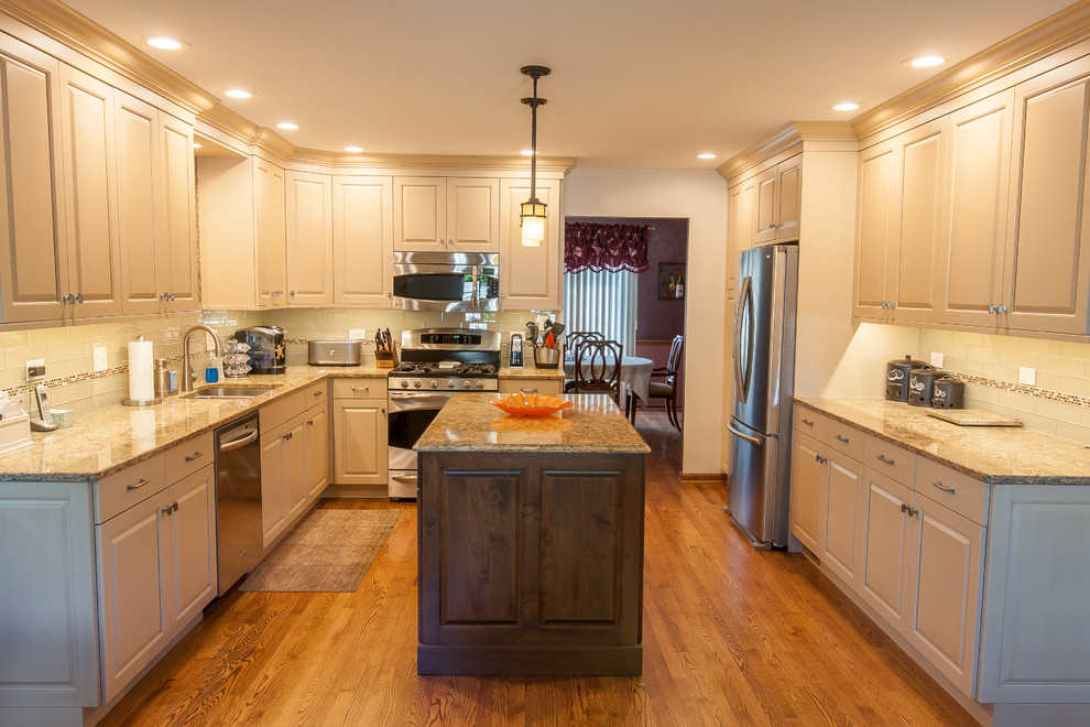 Photo of a mid-sized transitional u-shaped separate kitchen in Chicago with a double-bowl sink, raised-panel cabinets, white cabinets, white splashback, glass tile splashback, stainless steel appliances, medium hardwood floors, with island, brown floor and quartzite benchtops.