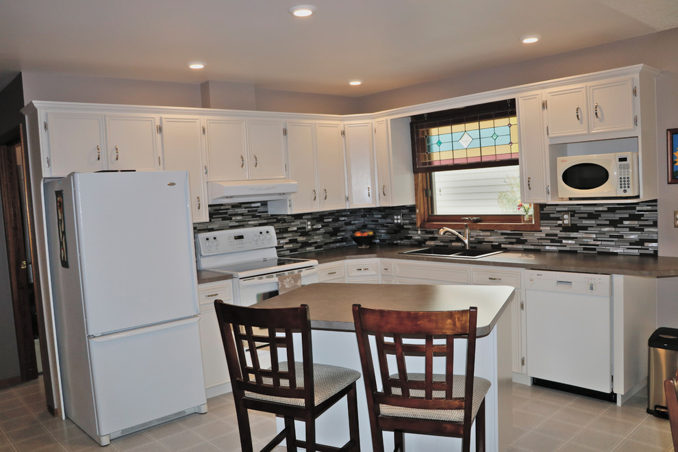 Example of a transitional l-shaped kitchen design with white cabinets, laminate countertops, glass tile backsplash, white appliances and an island