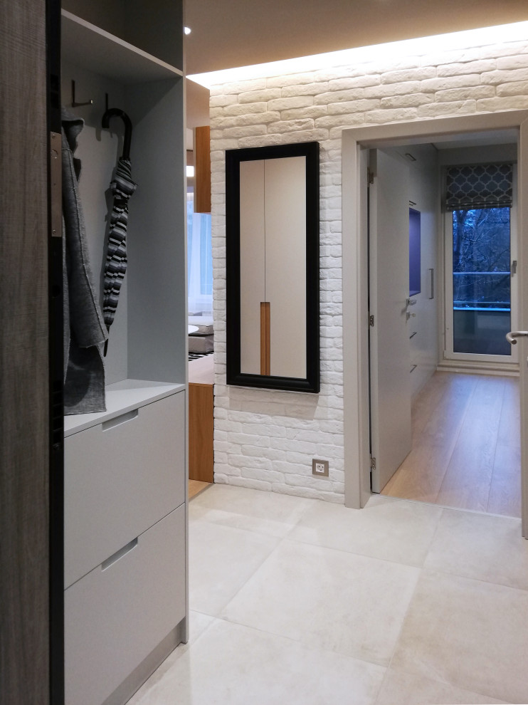 Photo of a small contemporary foyer in Other with grey walls, ceramic floors, grey floor and brick walls.