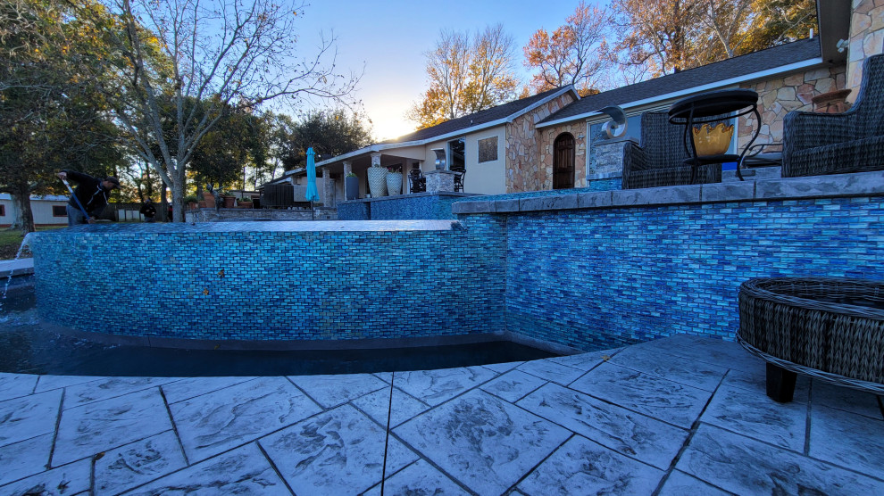 Diseño de piscina marinera extra grande redondeada en patio trasero con paisajismo de piscina y suelo de hormigón estampado