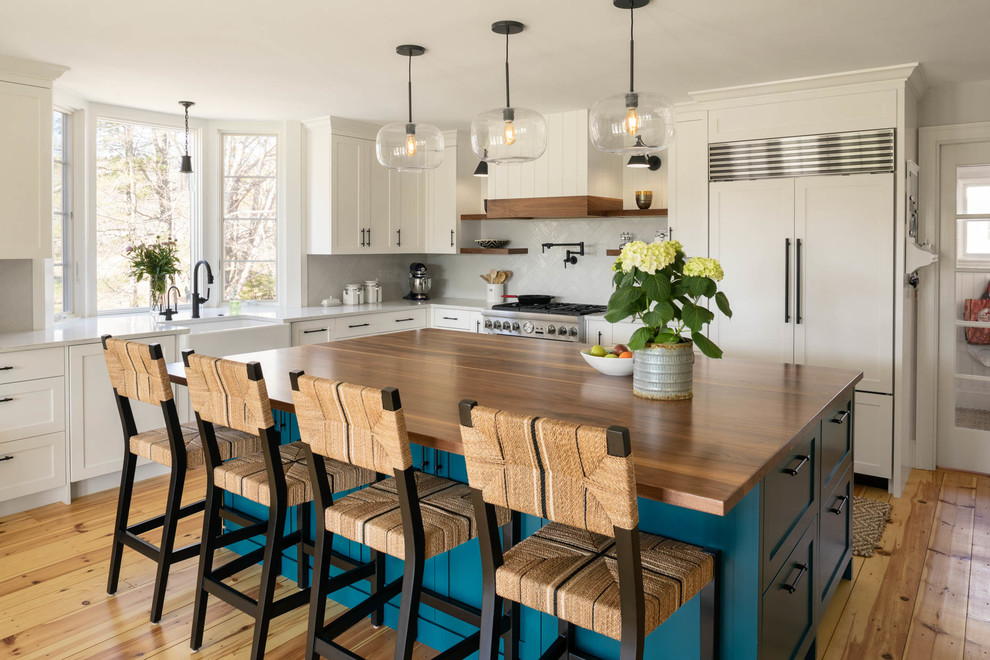 Design ideas for a beach style l-shaped kitchen in Portland Maine with a farmhouse sink, shaker cabinets, white cabinets, grey splashback, panelled appliances, light hardwood floors, with island and grey benchtop.