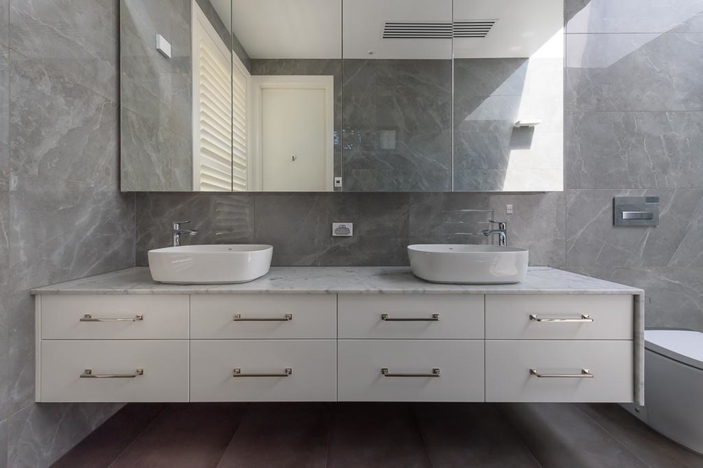 Photo of a large modern bathroom in Melbourne with flat-panel cabinets, white cabinets, an open shower, a one-piece toilet, gray tile, porcelain tile, grey walls, porcelain floors, a vessel sink, marble benchtops, grey floor, an open shower and multi-coloured benchtops.