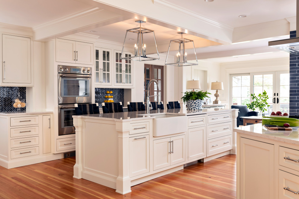 Mid-sized transitional u-shaped medium tone wood floor, brown floor and coffered ceiling eat-in kitchen photo in Boston with beaded inset cabinets, white cabinets, granite countertops, stainless steel appliances, a farmhouse sink, blue backsplash, matchstick tile backsplash, an island and multicolored countertops