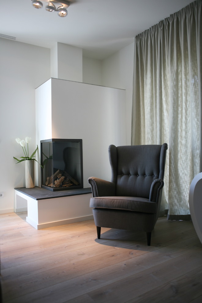 Photo of a small contemporary family room in Berlin with white walls, light hardwood floors and a corner fireplace.