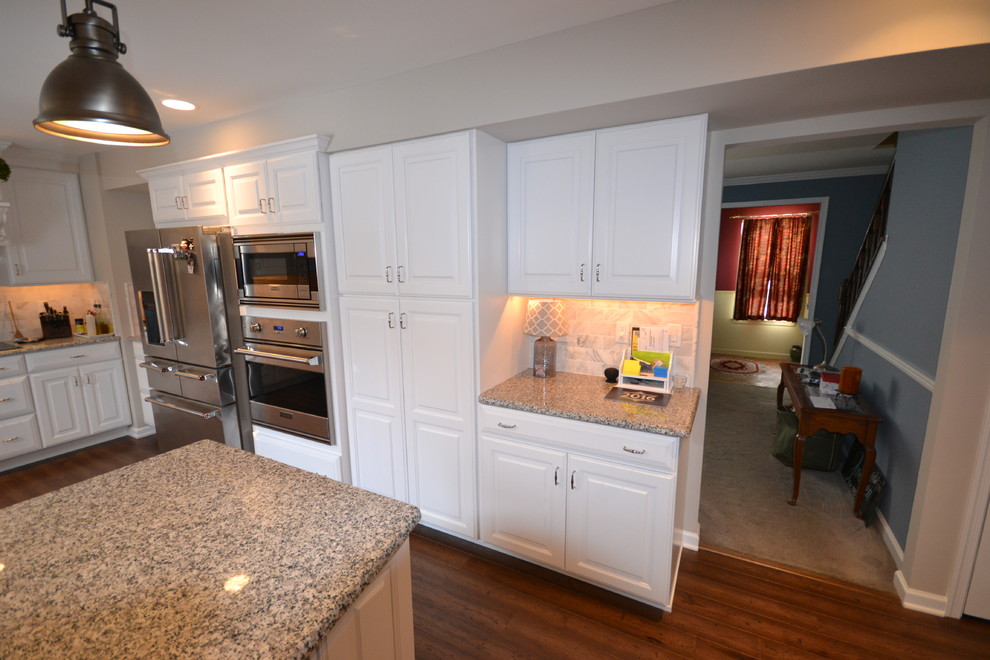 Photo of a large traditional l-shaped eat-in kitchen in Philadelphia with a farmhouse sink, raised-panel cabinets, white cabinets, granite benchtops, beige splashback, ceramic splashback, stainless steel appliances, medium hardwood floors and with island.