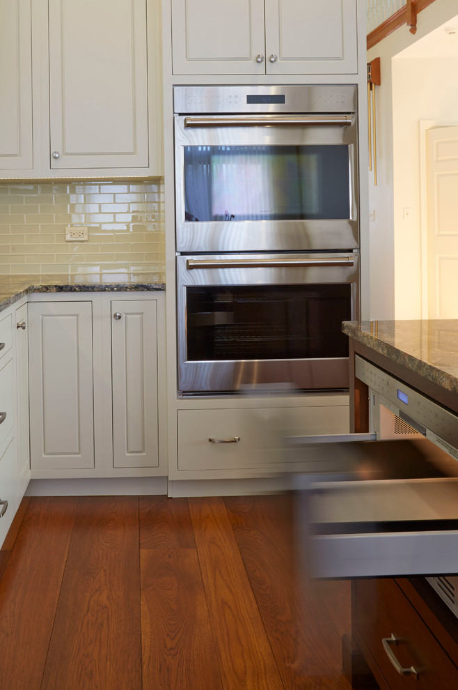 Inspiration for a mid-sized transitional u-shaped medium tone wood floor enclosed kitchen remodel in Chicago with a single-bowl sink, raised-panel cabinets, white cabinets, granite countertops, white backsplash, glass tile backsplash, stainless steel appliances and an island