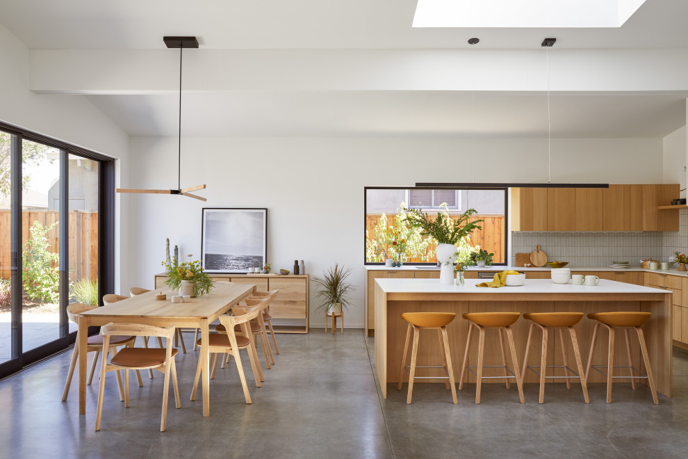 Large minimalist l-shaped concrete floor, gray floor and exposed beam open concept kitchen photo in San Francisco with an undermount sink, flat-panel cabinets, light wood cabinets, white backsplash, ceramic backsplash, stainless steel appliances, an island and white countertops