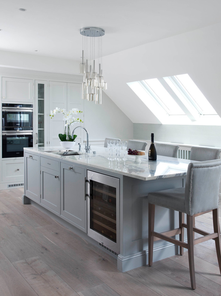 This is an example of a large transitional kitchen in Dublin with recessed-panel cabinets, white cabinets, light hardwood floors and with island.