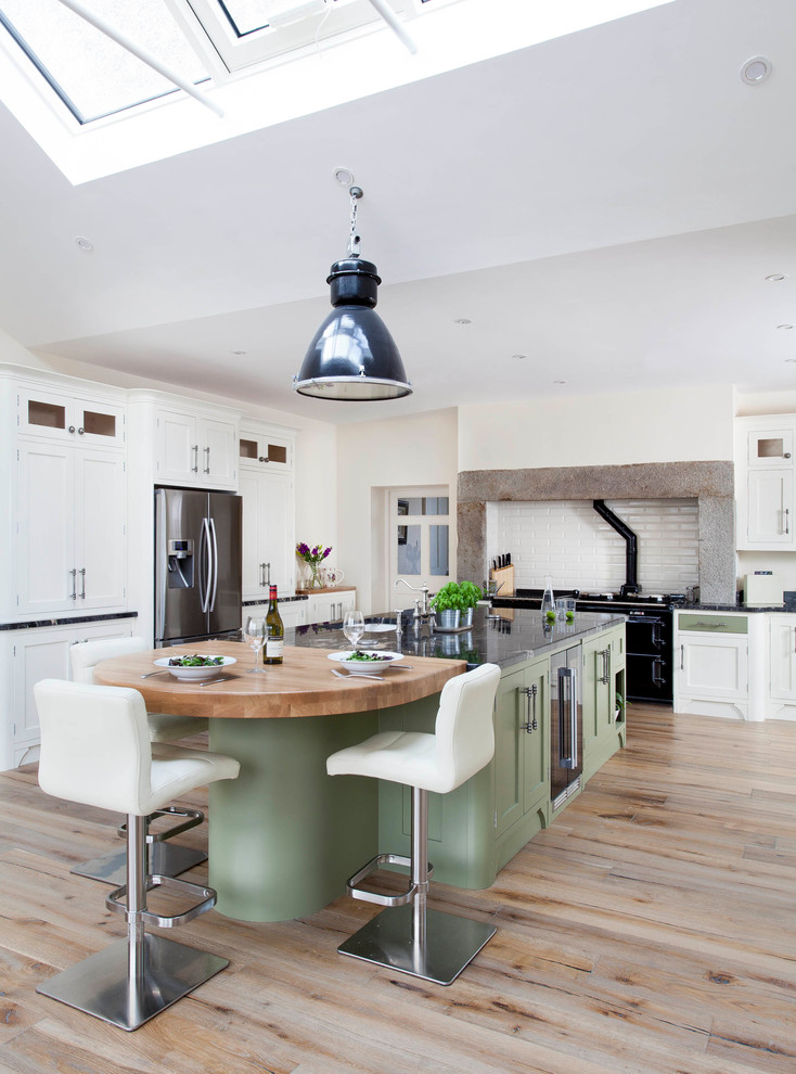 This is an example of a large country l-shaped eat-in kitchen in Belfast with an undermount sink, shaker cabinets, green cabinets, granite benchtops, white splashback, ceramic splashback, stainless steel appliances, light hardwood floors, with island and brown floor.