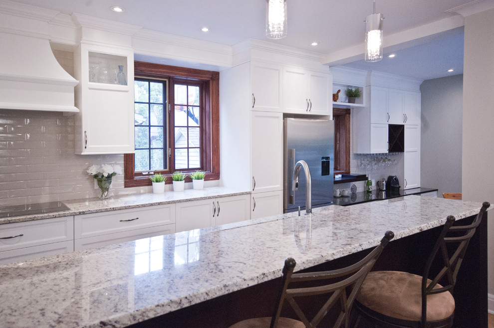 Eat-in kitchen - mid-sized transitional galley ceramic tile eat-in kitchen idea in Montreal with an undermount sink, shaker cabinets, white cabinets, granite countertops, beige backsplash, subway tile backsplash, stainless steel appliances and an island