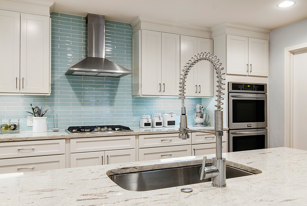 This is an example of a mid-sized traditional l-shaped eat-in kitchen in Dallas with an undermount sink, shaker cabinets, white cabinets, granite benchtops, blue splashback, glass tile splashback, stainless steel appliances and light hardwood floors.