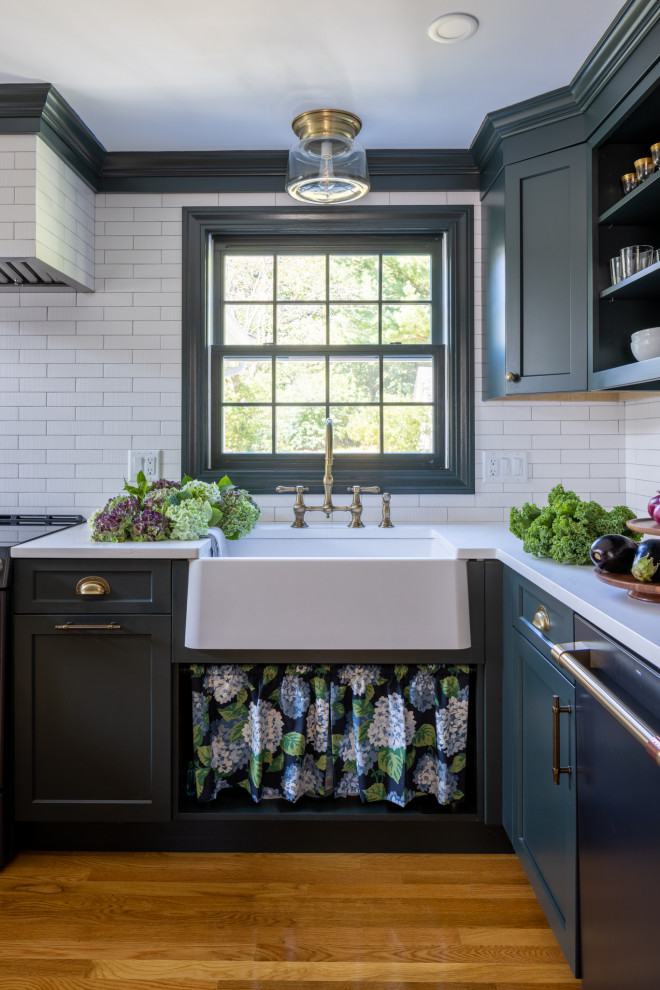 Inspiration for a transitional u-shaped medium tone wood floor and brown floor kitchen remodel in Boston with a farmhouse sink, shaker cabinets, green cabinets, quartz countertops, white backsplash, ceramic backsplash, black appliances, a peninsula and white countertops