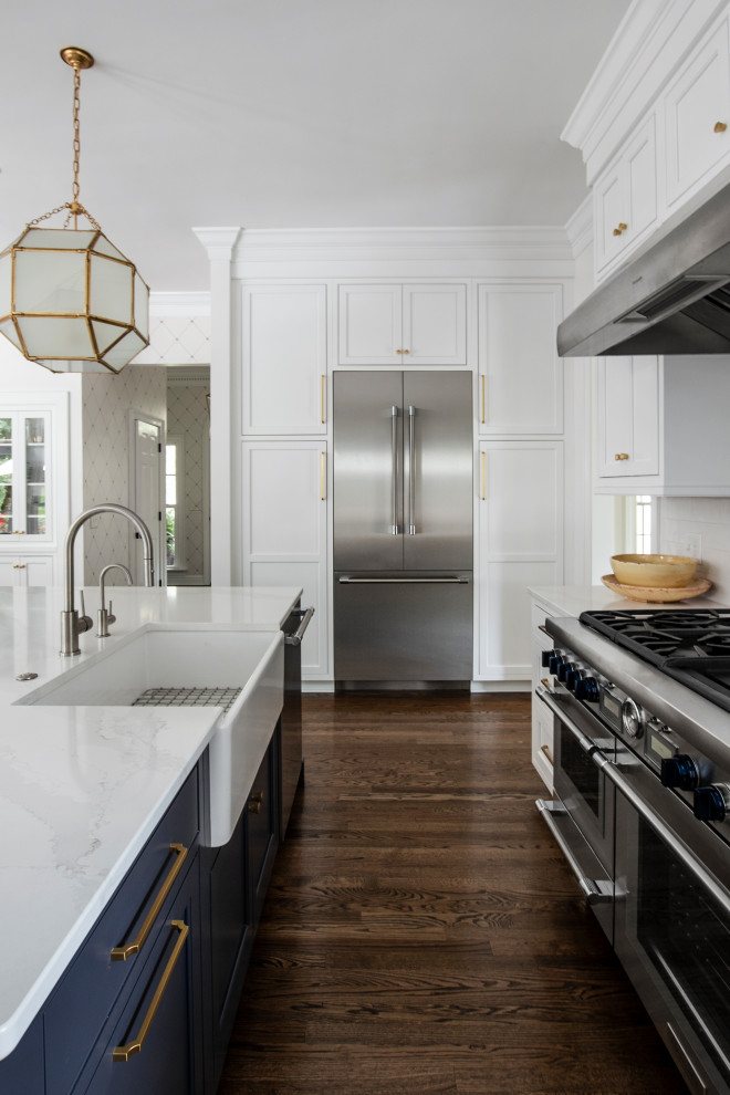 Large transitional u-shaped eat-in kitchen in Nashville with a farmhouse sink, beaded inset cabinets, white cabinets, quartz benchtops, white splashback, ceramic splashback, stainless steel appliances, dark hardwood floors, with island, brown floor and white benchtop.