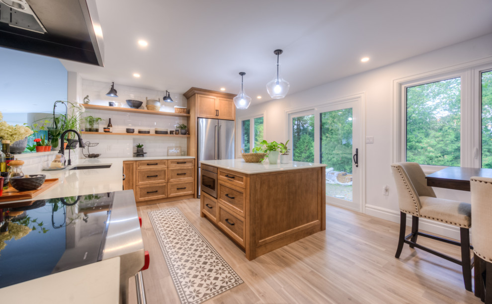 Example of a transitional l-shaped kitchen design in Toronto with an undermount sink, shaker cabinets, light wood cabinets, white backsplash, stainless steel appliances, an island and white countertops