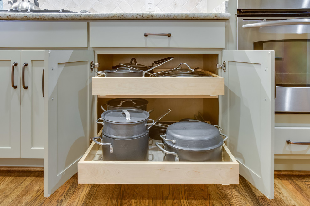 Inspiration for a transitional u-shaped medium tone wood floor and brown floor enclosed kitchen remodel in Birmingham with a double-bowl sink, shaker cabinets, beige cabinets, granite countertops, beige backsplash, travertine backsplash, stainless steel appliances and an island