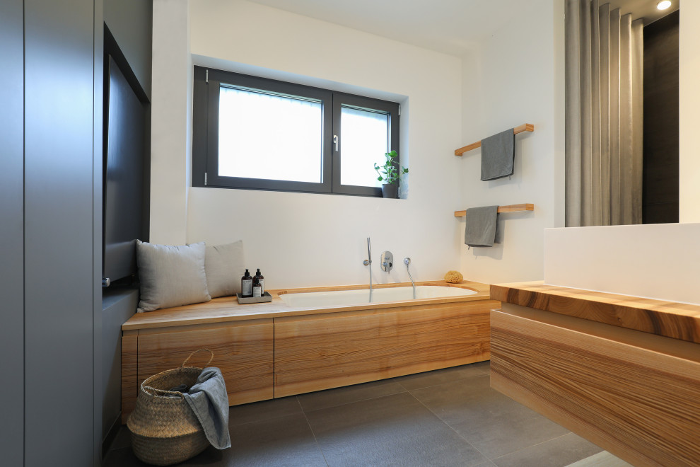 Mid-sized contemporary master bathroom in Frankfurt with flat-panel cabinets, light wood cabinets, an undermount tub, a curbless shower, a one-piece toilet, gray tile, white walls, a vessel sink, solid surface benchtops, grey floor, a shower curtain, a double vanity, a floating vanity and brown benchtops.