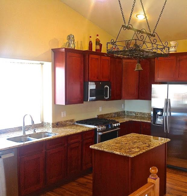 Example of a mid-sized transitional l-shaped medium tone wood floor eat-in kitchen design in Denver with an undermount sink, recessed-panel cabinets, distressed cabinets, granite countertops, beige backsplash, stone slab backsplash, stainless steel appliances and an island