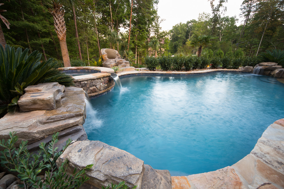 Inspiration for an expansive tropical backyard custom-shaped pool in Charlotte with natural stone pavers and a hot tub.