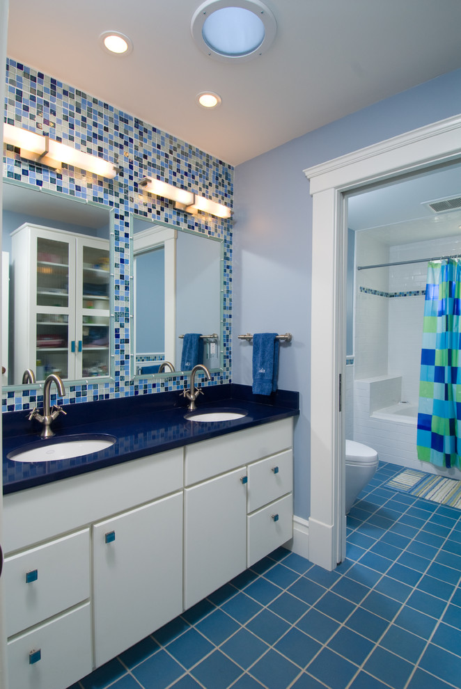Mid-sized traditional kids bathroom in Detroit with white cabinets, blue tile, mosaic tile, flat-panel cabinets, an alcove tub, a shower/bathtub combo, a two-piece toilet, blue walls, ceramic floors, an undermount sink, solid surface benchtops, blue floor and blue benchtops.