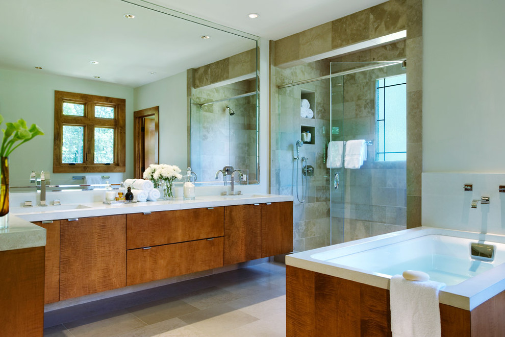 This is an example of a modern master bathroom in Other with flat-panel cabinets, a drop-in tub, an alcove shower, a two-piece toilet, travertine floors, an integrated sink, concrete benchtops, a hinged shower door, brown cabinets, beige tile, marble, beige walls, beige floor, white benchtops, a double vanity and a floating vanity.