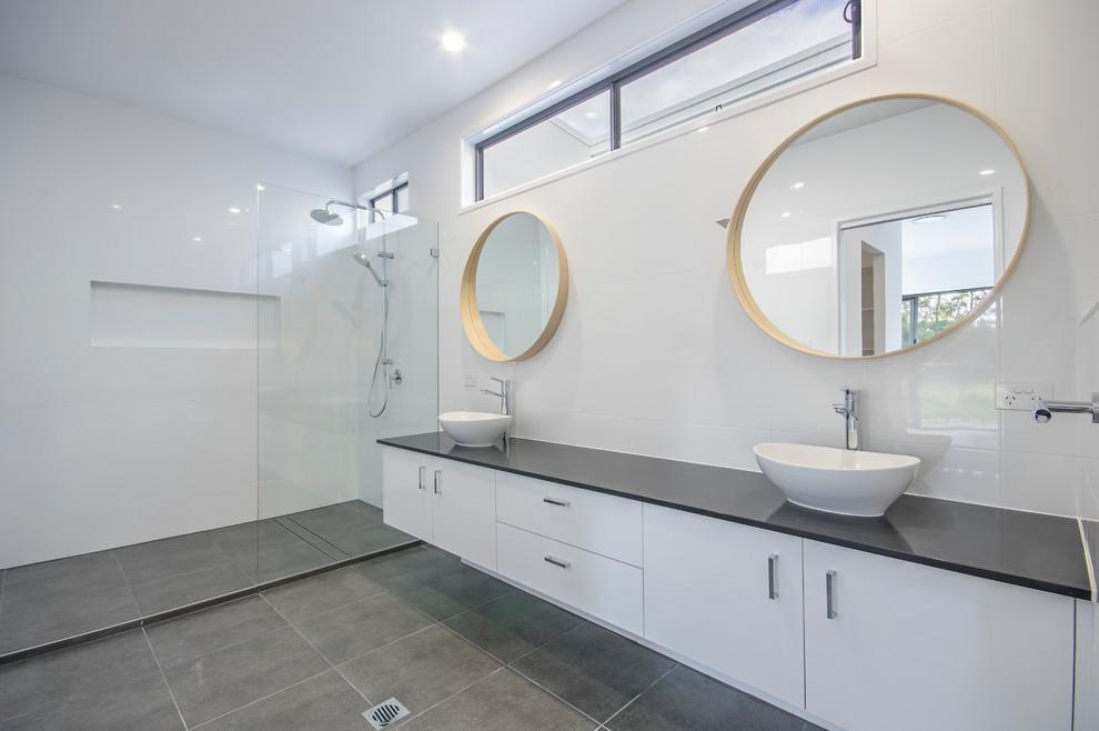 This is an example of a large contemporary master bathroom in Sunshine Coast with white cabinets, an open shower, a one-piece toilet, white tile, porcelain tile, white walls, porcelain floors, a vessel sink, engineered quartz benchtops, grey floor, an open shower and black benchtops.