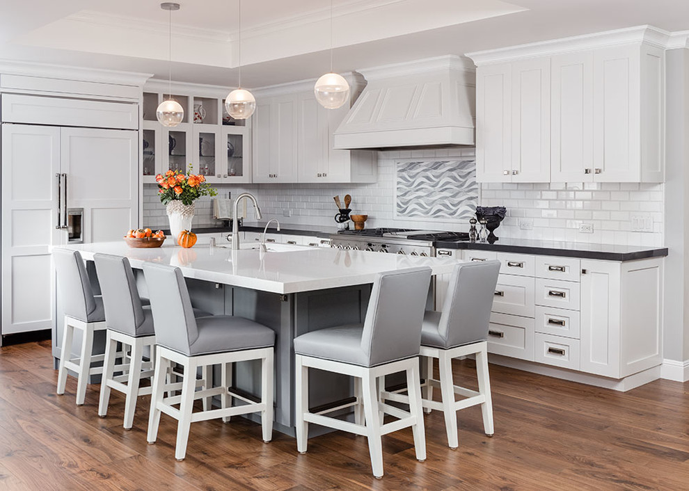Design ideas for a mid-sized transitional l-shaped open plan kitchen in San Francisco with white cabinets, quartz benchtops, white splashback, stainless steel appliances, with island, an undermount sink, shaker cabinets, subway tile splashback, dark hardwood floors and brown floor.