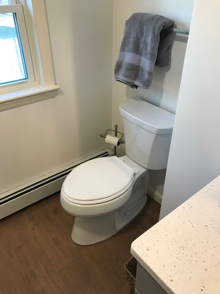 Inspiration for a mid-sized transitional powder room in Boston with shaker cabinets, grey cabinets, a two-piece toilet, white walls, vinyl floors, an undermount sink, engineered quartz benchtops, brown floor and white benchtops.