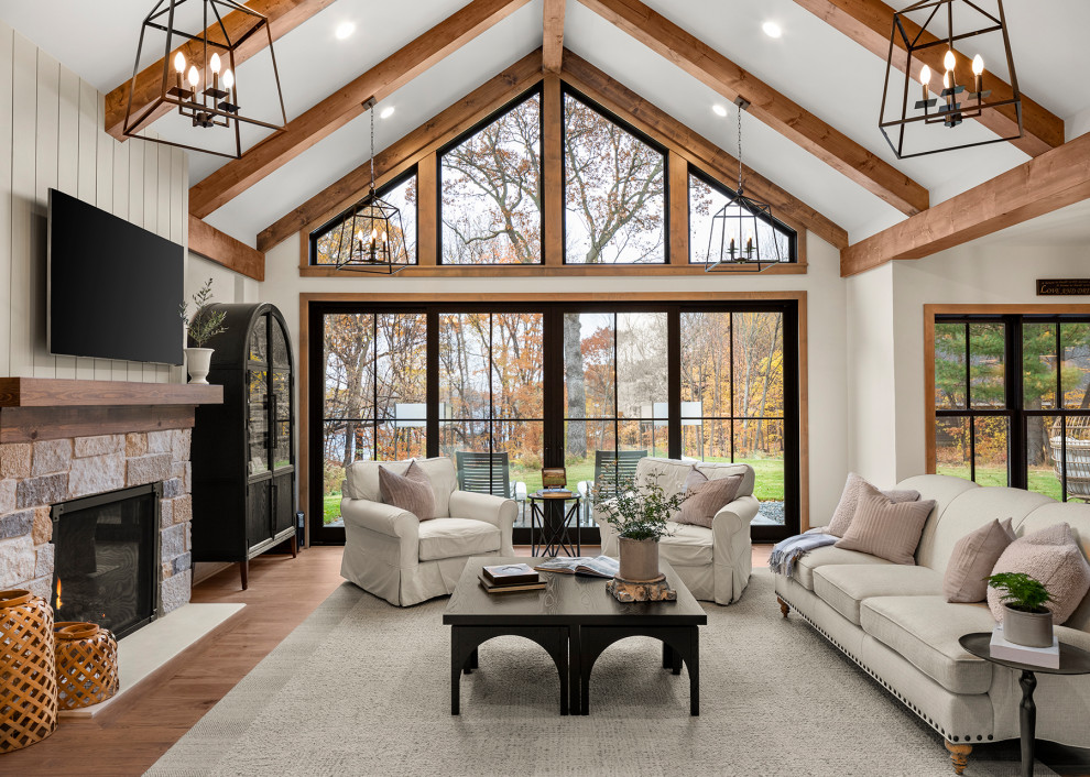 This is an example of a large beach style open concept family room in Minneapolis with medium hardwood floors, a standard fireplace, a stone fireplace surround, a wall-mounted tv, brown floor and vaulted.