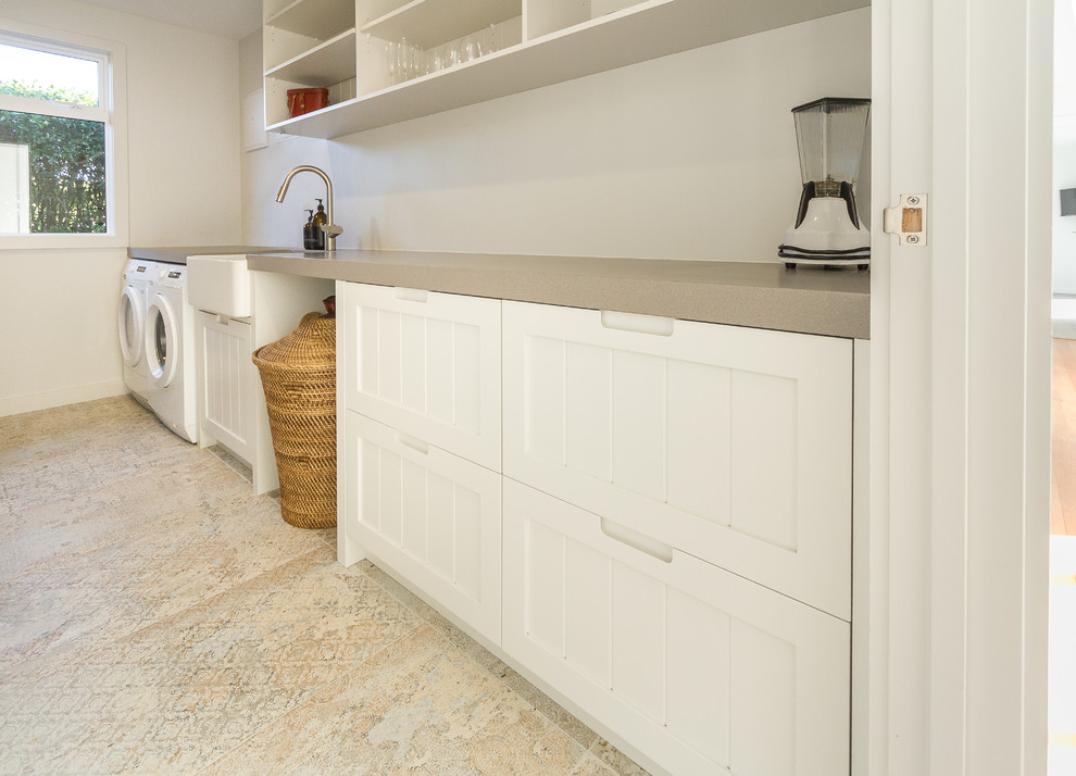 Small traditional galley utility room in Napier-Hastings with a farmhouse sink, recessed-panel cabinets, white cabinets, quartz benchtops, white walls, ceramic floors, a side-by-side washer and dryer, multi-coloured floor and grey benchtop.