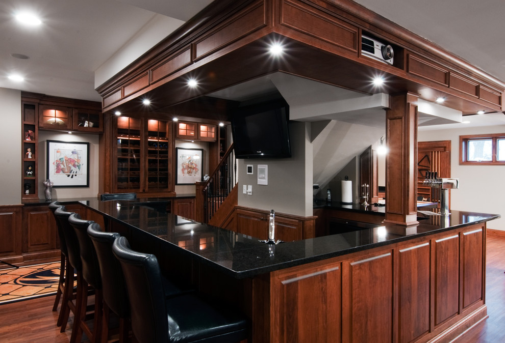 Large traditional u-shaped seated home bar in Chicago with raised-panel cabinets, medium wood cabinets, granite benchtops, medium hardwood floors and brown floor.