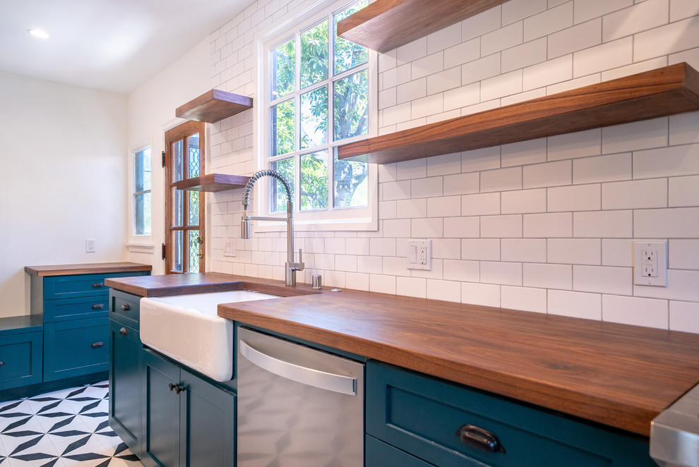 This is an example of a large mediterranean galley open plan kitchen in Los Angeles with a farmhouse sink, shaker cabinets, blue cabinets, wood benchtops, white splashback, subway tile splashback, stainless steel appliances, porcelain floors, with island, multi-coloured floor and brown benchtop.