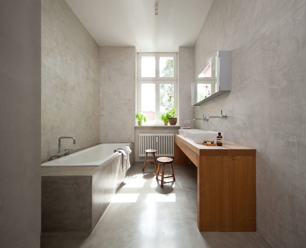 This is an example of a mid-sized modern bathroom in Berlin with a drop-in tub, grey walls, concrete floors, a vessel sink, wood benchtops and brown benchtops.