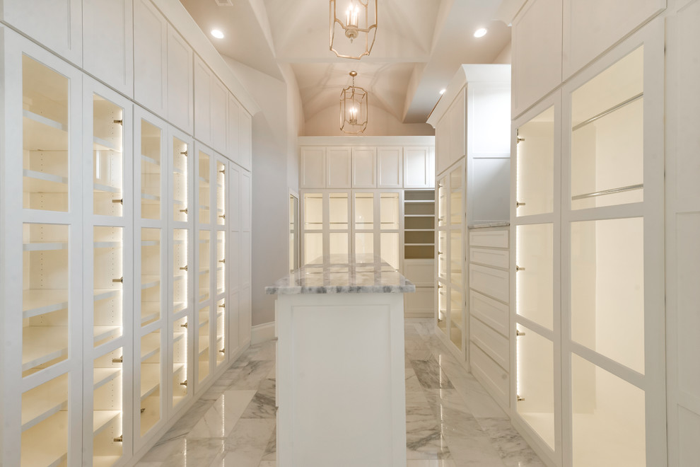 This is an example of a large gender-neutral walk-in wardrobe in Dallas with glass-front cabinets, white cabinets, marble floors and grey floor.