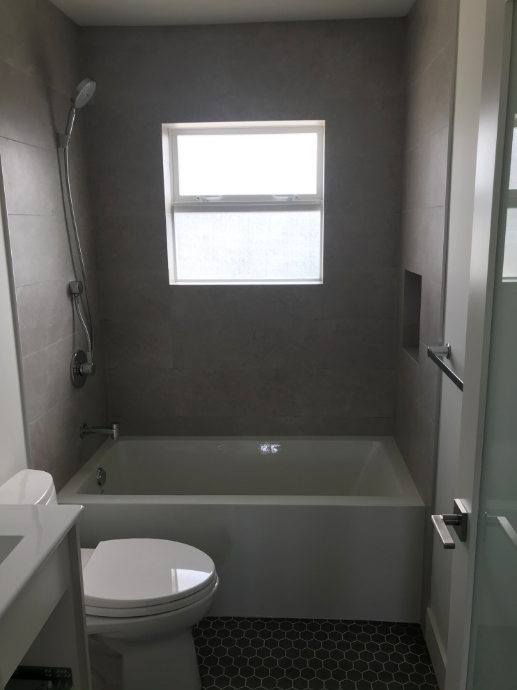 На фото: главная, серо-белая ванная комната среднего размера в стиле модернизм с ванной в нише, серой плиткой, керамогранитной плиткой, полом из мозаичной плитки, черным полом, нишей, белыми фасадами, душем над ванной, унитазом-моноблоком, белыми стенами, врезной раковиной, столешницей из искусственного камня, открытым душем, белой столешницей, тумбой под одну раковину и напольной тумбой