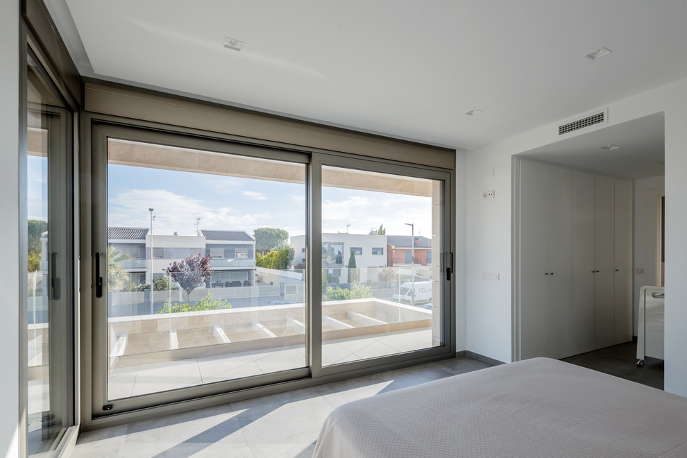 Modelo de dormitorio principal minimalista grande con paredes blancas, suelo de baldosas de porcelana y suelo gris