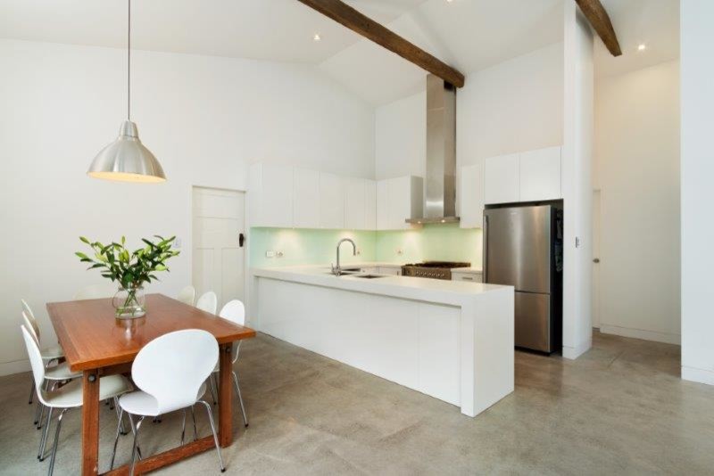 This is an example of a small contemporary one-storey u-shaped eat-in kitchen in Sydney with an undermount sink, white cabinets, quartz benchtops, white splashback, glass sheet splashback, stainless steel appliances, concrete floors and with island.