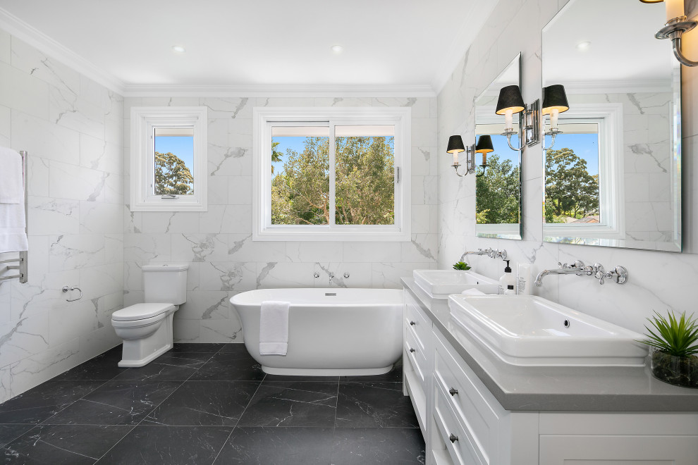 Design ideas for a large beach style master bathroom in Sydney with shaker cabinets, white cabinets, white tile, marble, white walls, marble floors, a console sink, black floor, grey benchtops, a freestanding tub, a two-piece toilet, a double vanity and a freestanding vanity.