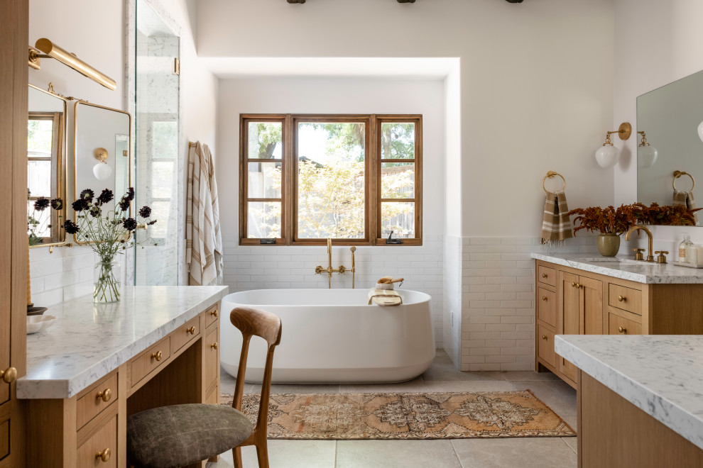 Inspiration for a cottage master subway tile beige floor and double-sink freestanding bathtub remodel in Sacramento with shaker cabinets, medium tone wood cabinets, white walls, an undermount sink, marble countertops, multicolored countertops and a built-in vanity