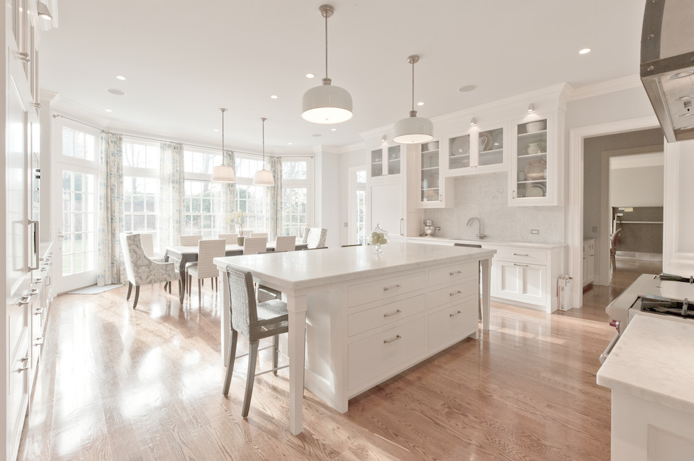 Photo of a traditional eat-in kitchen in New York with marble benchtops, white splashback, stone slab splashback, white cabinets and recessed-panel cabinets.