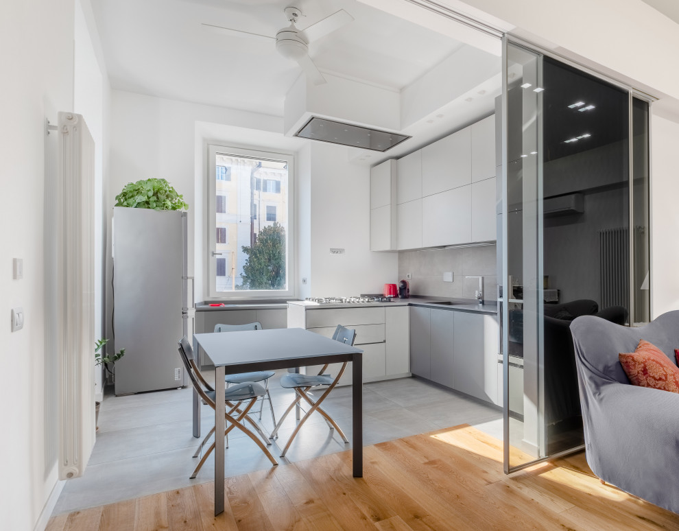 Expansive contemporary l-shaped eat-in kitchen in Rome with an undermount sink, flat-panel cabinets, grey cabinets, marble benchtops, grey splashback, porcelain splashback, black appliances, porcelain floors, a peninsula, grey floor, grey benchtop and recessed.
