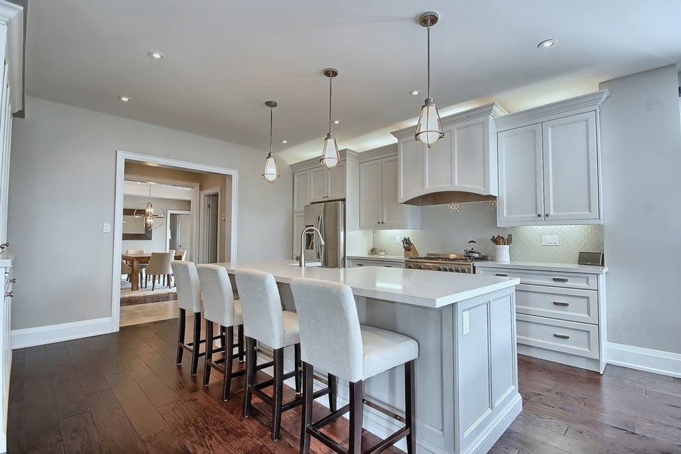 Mid-sized traditional single-wall open plan kitchen in Toronto with a farmhouse sink, beaded inset cabinets, white cabinets, quartz benchtops, white splashback, porcelain splashback, stainless steel appliances, dark hardwood floors and with island.