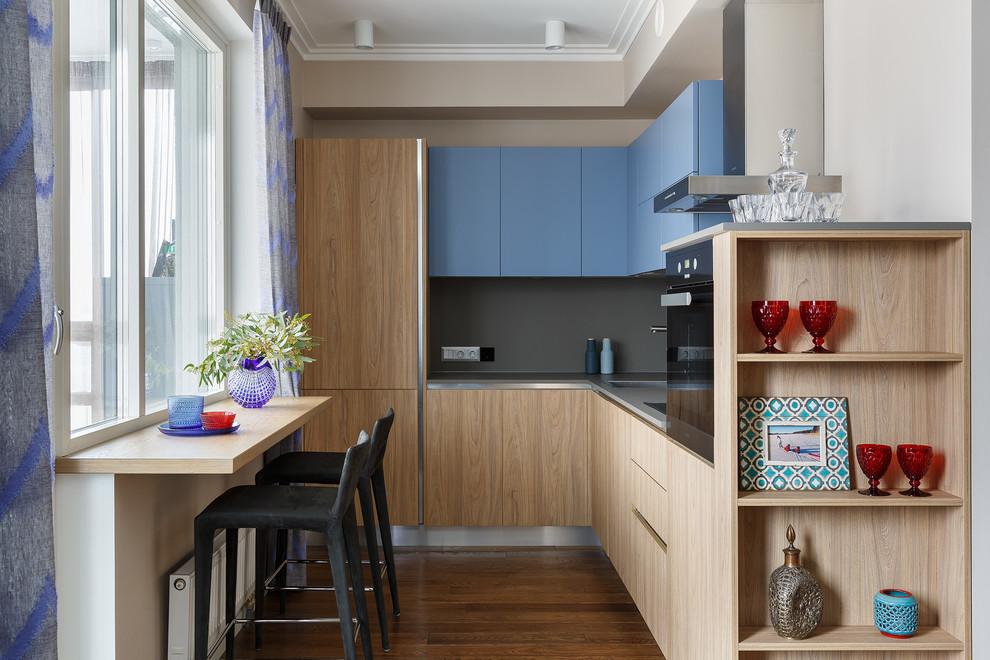 Inspiration for a mid-sized contemporary l-shaped open plan kitchen in Saint Petersburg with flat-panel cabinets, medium hardwood floors, no island, a drop-in sink, grey splashback, brown floor, grey benchtop, blue cabinets and panelled appliances.