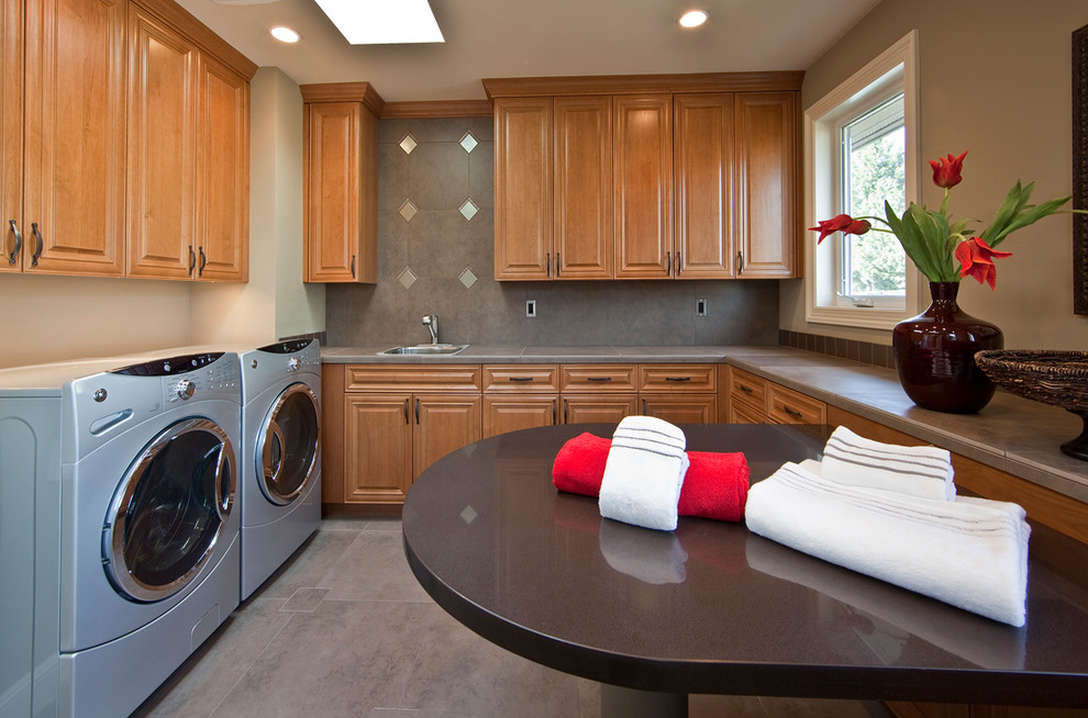 This is an example of a large traditional u-shaped dedicated laundry room in Seattle with raised-panel cabinets, medium wood cabinets, a side-by-side washer and dryer, a drop-in sink, grey floor, concrete benchtops, beige walls, concrete floors and grey benchtop.
