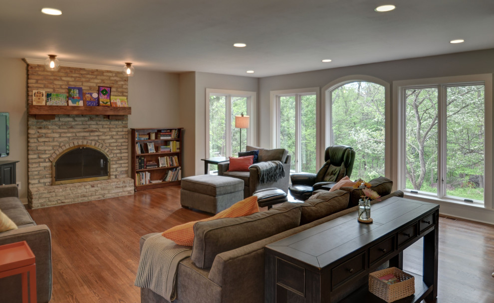 Inspiration for a mid-sized country open concept family room in Columbus with grey walls, medium hardwood floors, a standard fireplace, a brick fireplace surround and a freestanding tv.